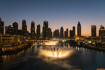 Image showing Dubai singing fountains at night lake view between skyscrapers. City skyline in dusk modern architecture in UAE capital downtown.