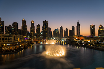 Image showing Dubai singing fountains at night lake view between skyscrapers. City skyline in dusk modern architecture in UAE capital downtown.