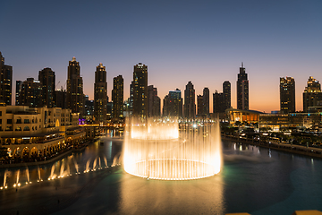 Image showing Dubai singing fountains at night lake view between skyscrapers. City skyline in dusk modern architecture in UAE capital downtown.