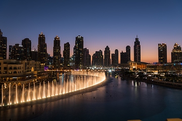 Image showing Dubai singing fountains at night lake view between skyscrapers. City skyline in dusk modern architecture in UAE capital downtown.