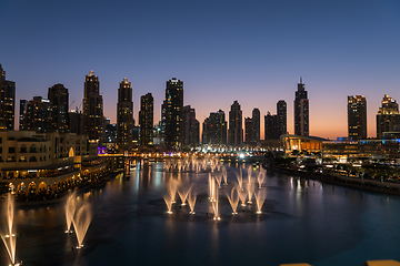 Image showing Dubai singing fountains at night lake view between skyscrapers. City skyline in dusk modern architecture in UAE capital downtown.