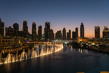 Image showing Dubai singing fountains at night lake view between skyscrapers. City skyline in dusk modern architecture in UAE capital downtown.