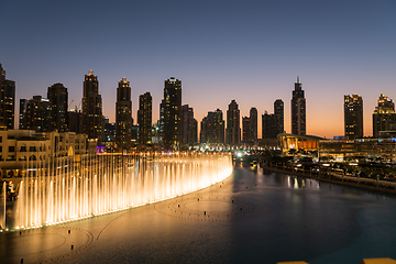 Image showing Dubai singing fountains at night lake view between skyscrapers. City skyline in dusk modern architecture in UAE capital downtown.