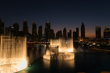 Image showing Dubai singing fountains at night lake view between skyscrapers. City skyline in dusk modern architecture in UAE capital downtown.