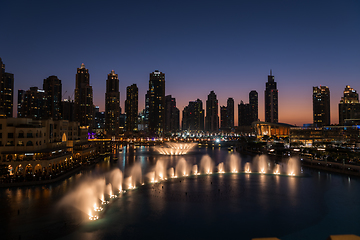 Image showing Dubai singing fountains at night lake view between skyscrapers. City skyline in dusk modern architecture in UAE capital downtown.