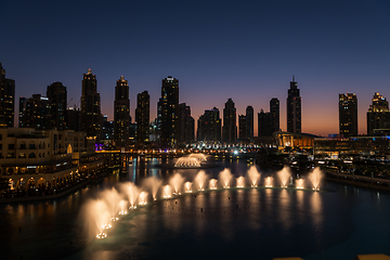 Image showing Dubai singing fountains at night lake view between skyscrapers. City skyline in dusk modern architecture in UAE capital downtown.