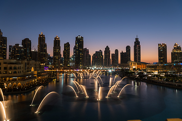 Image showing Dubai singing fountains at night lake view between skyscrapers. City skyline in dusk modern architecture in UAE capital downtown.