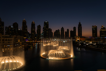 Image showing Dubai singing fountains at night lake view between skyscrapers. City skyline in dusk modern architecture in UAE capital downtown.