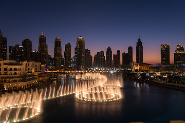 Image showing Dubai singing fountains at night lake view between skyscrapers. City skyline in dusk modern architecture in UAE capital downtown.