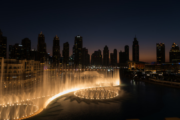 Image showing Dubai singing fountains at night lake view between skyscrapers. City skyline in dusk modern architecture in UAE capital downtown.