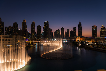 Image showing Dubai singing fountains at night lake view between skyscrapers. City skyline in dusk modern architecture in UAE capital downtown.