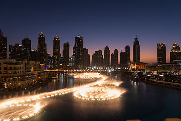 Image showing Dubai singing fountains at night lake view between skyscrapers. City skyline in dusk modern architecture in UAE capital downtown.