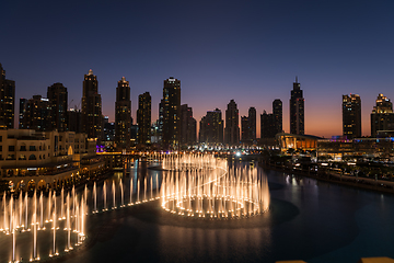 Image showing Dubai singing fountains at night lake view between skyscrapers. City skyline in dusk modern architecture in UAE capital downtown.