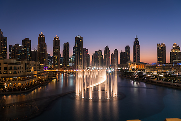 Image showing Dubai singing fountains at night lake view between skyscrapers. City skyline in dusk modern architecture in UAE capital downtown.