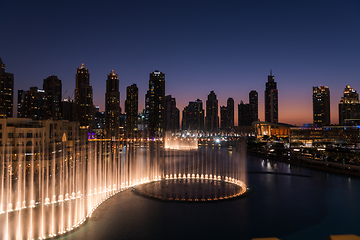 Image showing Dubai singing fountains at night lake view between skyscrapers. City skyline in dusk modern architecture in UAE capital downtown.