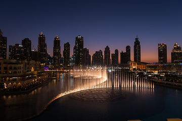 Image showing Dubai singing fountains at night lake view between skyscrapers. City skyline in dusk modern architecture in UAE capital downtown.