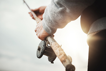 Image showing Hands, fishing and rod with a man in nature, enjoying a weekend trip his hobby or pastime at sunset. Morning, flare and low angle with a male fisherman casting a line outdoor in the wilderness