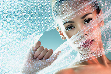 Image showing Bubble wrap, beauty and portrait of woman with makeup, cosmetics and skincare products in studio. Creative art, salon aesthetic and girl with face glow, lipstick and luxury style with plastic tear