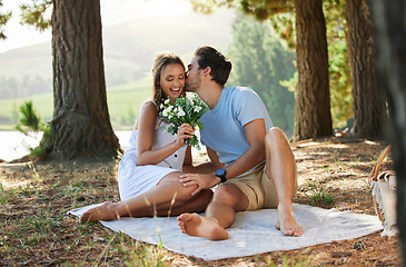 Image showing Couple kiss, love and flowers on picnic, summer with freedom and adventure, affection in relationship and care outdoor. Happy people together in nature, commitment and trust with romance in forest