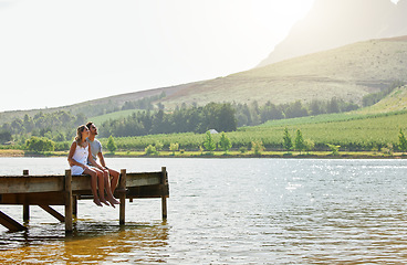 Image showing Couple in nature, relax by lake and summer, travel and adventure, love and care outdoor. People in relationship, trust and bond on vacation, man and woman together sitting on jetty, freedom and view