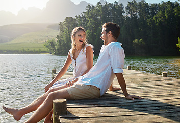 Image showing Love, laugh and pier with couple at lake for bonding, romance and affectionate date. Nature, travel and holiday with man and woman sitting on boardwalk in countryside for happy, summer and vacation