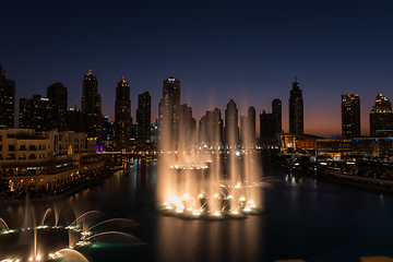 Image showing Dubai singing fountains at night lake view between skyscrapers. City skyline in dusk modern architecture in UAE capital downtown.