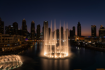 Image showing Dubai singing fountains at night lake view between skyscrapers. City skyline in dusk modern architecture in UAE capital downtown.