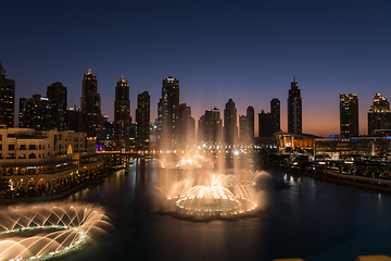 Image showing Dubai singing fountains at night lake view between skyscrapers. City skyline in dusk modern architecture in UAE capital downtown.