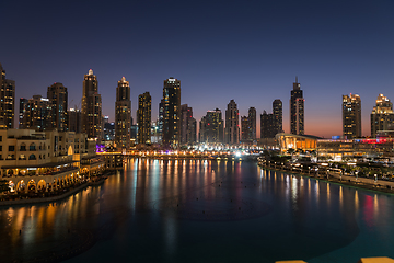 Image showing Dubai singing fountains at night lake view between skyscrapers. City skyline in dusk modern architecture in UAE capital downtown.