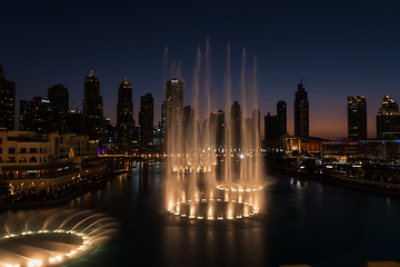 Image showing Dubai singing fountains at night lake view between skyscrapers. City skyline in dusk modern architecture in UAE capital downtown.