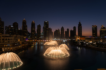 Image showing Dubai singing fountains at night lake view between skyscrapers. City skyline in dusk modern architecture in UAE capital downtown.