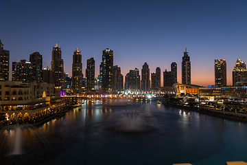 Image showing Dubai singing fountains at night lake view between skyscrapers. City skyline in dusk modern architecture in UAE capital downtown.