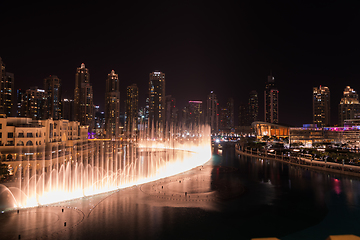 Image showing Dubai singing fountains at night lake view between skyscrapers. City skyline in dusk modern architecture in UAE capital downtown.