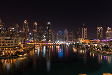 Image showing Dubai singing fountains at night lake view between skyscrapers. City skyline in dusk modern architecture in UAE capital downtown.