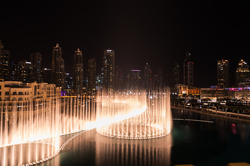 Image showing Dubai singing fountains at night lake view between skyscrapers. City skyline in dusk modern architecture in UAE capital downtown.