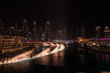 Image showing Dubai singing fountains at night lake view between skyscrapers. City skyline in dusk modern architecture in UAE capital downtown.