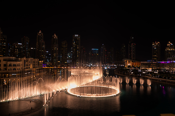 Image showing Dubai singing fountains at night lake view between skyscrapers. City skyline in dusk modern architecture in UAE capital downtown.