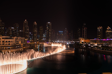 Image showing Dubai singing fountains at night lake view between skyscrapers. City skyline in dusk modern architecture in UAE capital downtown.