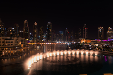 Image showing Dubai singing fountains at night lake view between skyscrapers. City skyline in dusk modern architecture in UAE capital downtown.