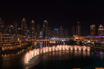 Image showing Dubai singing fountains at night lake view between skyscrapers. City skyline in dusk modern architecture in UAE capital downtown.