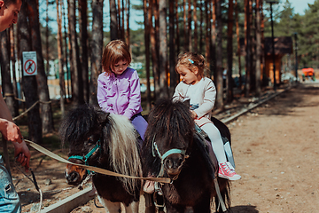 Image showing Two little girls having fun in the park while riding small horses