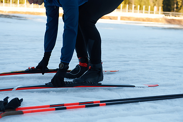 Image showing Handsome male athlete with cross country skis preparing equipment for training in a snowy forest. Checking smartwatch. Healthy winter lifestyle.