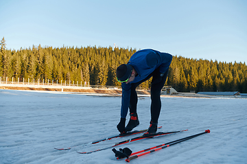 Image showing Handsome male athlete with cross country skis preparing equipment for training in a snowy forest. Checking smartwatch. Healthy winter lifestyle.