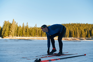 Image showing Handsome male athlete with cross country skis preparing equipment for training in a snowy forest. Checking smartwatch. Healthy winter lifestyle.