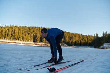 Image showing Handsome male athlete with cross country skis preparing equipment for training in a snowy forest. Checking smartwatch. Healthy winter lifestyle.