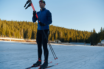 Image showing Handsome male athlete with cross country skis preparing equipment for training in a snowy forest. Checking smartwatch. Healthy winter lifestyle.