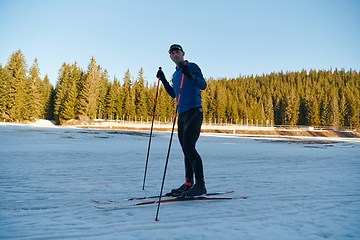 Image showing Handsome male athlete with cross country skis preparing equipment for training in a snowy forest. Checking smartwatch. Healthy winter lifestyle.