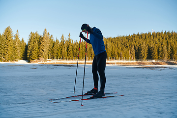 Image showing Handsome male athlete with cross country skis preparing equipment for training in a snowy forest. Checking smartwatch. Healthy winter lifestyle.