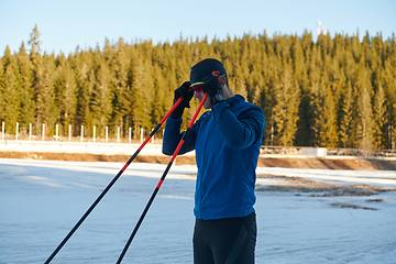 Image showing Handsome male athlete with cross country skis preparing equipment for training in a snowy forest. Checking smartwatch. Healthy winter lifestyle.