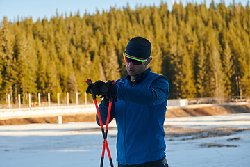 Image showing Handsome male athlete with cross country skis, taking fresh breath and having break after hard workout training in a snowy forest. Checking smartwatch. Healthy winter lifestyle